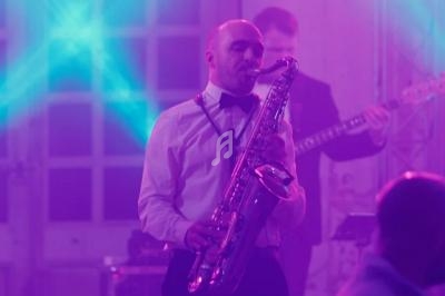 Un musicien en chemise blanche joue du saxophone sur une scène éclairée de lumières violettes et bleues.