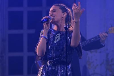 Une chanteuse en robe à paillettes bleues interprète une chanson sur scène, accompagnée d'un musicien à la basse.