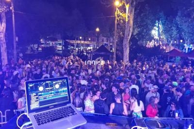 Vue depuis une scène avec un ordinateur portable affichant un logiciel DJ, face à une foule en soirée en plein air.