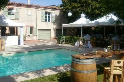 Jardin avec piscine, tables en bois, tonneaux et tentes blanches, décoré pour un événement en extérieur.