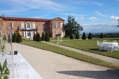 Grande bâtisse en briques rouges avec jardin aménagé, table dressée et vue dégagée sur un paysage rural.