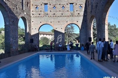 Ruines en briques entourant une piscine, avec des invités debout et un groupe de musique en arrière-plan.