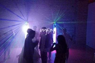 Des personnes dansent dans une salle sombre éclairée par des faisceaux lumineux colorés et des effets de fumée.