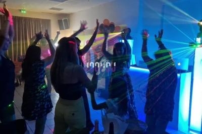 Des personnes dansent sous des lumières colorées et des lasers dans une ambiance festive en intérieur.