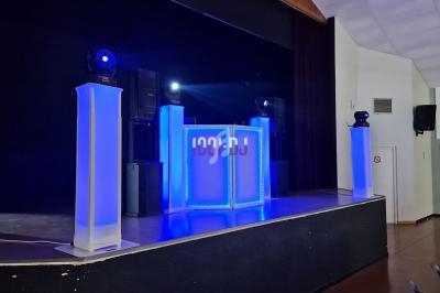 Scène équipée de colonnes lumineuses bleues, d'un pupitre éclairé et de projecteurs dans une salle de spectacle.