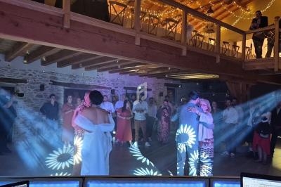 Un couple danse au centre d'une salle éclairée, entouré d'invités debout sous des lumières décoratives.