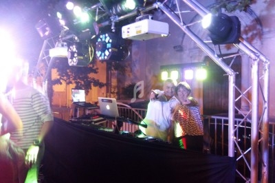 Un DJ anime une soirée en extérieur sous une structure lumineuse, accompagné d'une personne souriante.