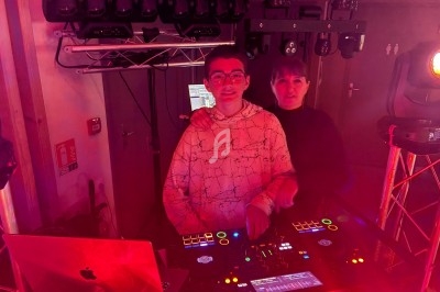 Deux personnes devant une table de mixage éclairée par des lumières rouges, entourées d'équipements de sonorisation.