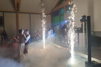Un couple danse au milieu de la fumée et des étincelles lors d'une réception dans une salle éclairée.