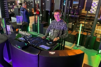 Un DJ souriant utilise une table de mixage dans un magasin équipé de matériel audio et d'éclairage.