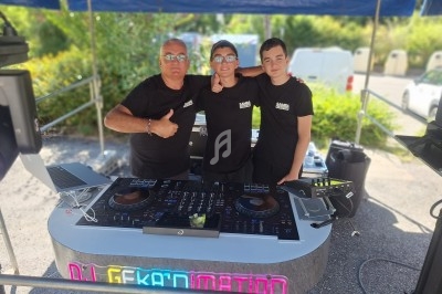 Trois personnes posent derrière une table de mixage sous un stand extérieur, entourées d'équipements audio.