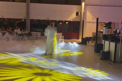 Un couple danse au centre d'une salle éclairée par des projecteurs jaunes, entouré de fumée au sol.