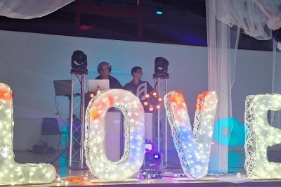 Deux DJ derrière des lettres lumineuses formant le mot ’LOVE’ dans une salle décorée pour un événement.