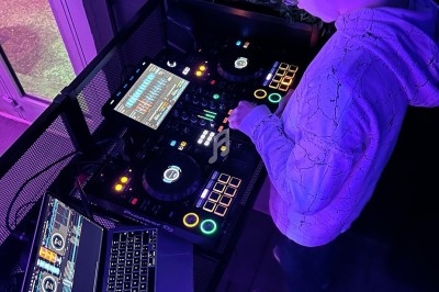 Un DJ mixe de la musique sur une console équipée d'écrans et d'un ordinateur portable dans un environnement lumineux.