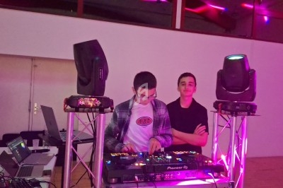 Deux personnes près d'une table de mixage avec des lumières colorées et des enceintes dans une salle.