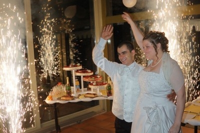 Un couple en tenue de mariage sourit et salue devant des fontaines d'étincelles dans une salle de réception.