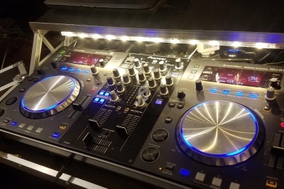 Table de mixage DJ avec éclairage LED, boutons, molettes et curseurs, posée sur un support dans un studio.