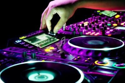 Main ajustant un bouton sur une console de mixage DJ éclairée par des lumières colorées.