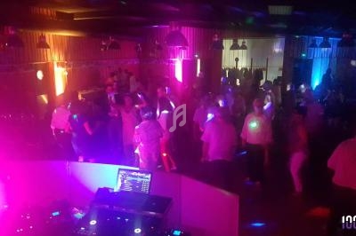 Salle obscure avec des lumières colorées et des personnes dansant près d'une table de mixage équipée d'un ordinateur.