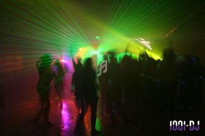 Personnes dansant dans une ambiance sombre avec des faisceaux lumineux colorés et des effets de laser.