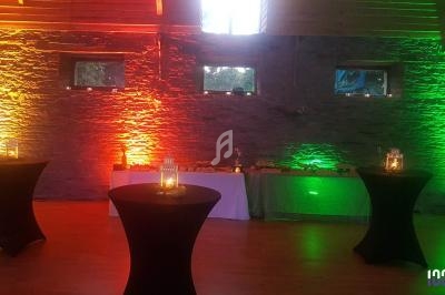 Salle décorée avec des lumières colorées, tables hautes noires et buffet installé le long d'un mur en pierre.