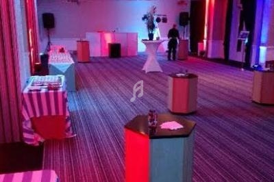 Salle de réception éclairée en rouge et bleu, avec tables hautes et équipements audio visibles en arrière-plan.