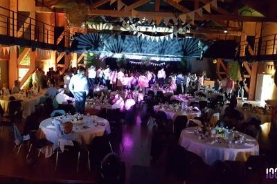 Salle de réception décorée avec des guirlandes, des tables dressées et des invités dansant sous des jeux de lumière.