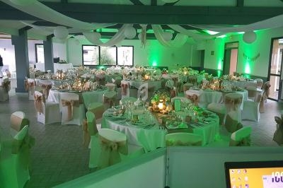 Salle de réception décorée pour un événement, avec tables rondes dressées, nappes blanches et éclairage vert.