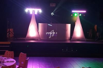 Salle de réception avec tables dressées et une scène équipée de lumières et matériel de sonorisation.