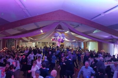 Salle décorée avec des guirlandes, remplie de personnes dansant et discutant lors d'un événement festif.