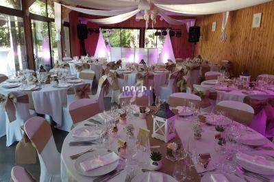 Salle de réception décorée pour un événement, avec tables rondes dressées, nappes blanches et éclairage rose.