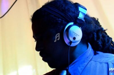 Un DJ portant un casque audio, éclairé par une lumière tamisée dans un environnement intérieur.