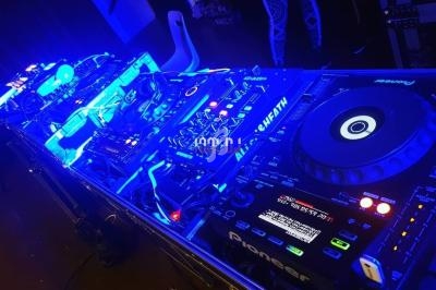 Table de mixage éclairée en bleu, équipée de platines et d'équipements audio professionnels dans un environnement sombre.