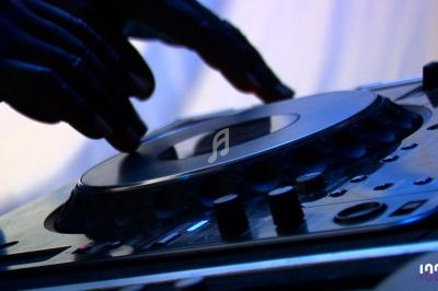 Main posée sur une platine de DJ en fonctionnement, avec des boutons et commandes visibles au premier plan.