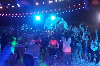 Groupe de personnes dansant sous des lumières colorées entourées de mousse lors d'une fête nocturne.