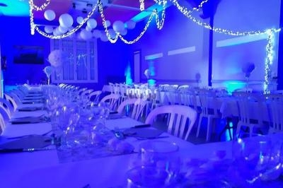 Salle de réception décorée avec des guirlandes lumineuses, des ballons suspendus et des tables dressées.