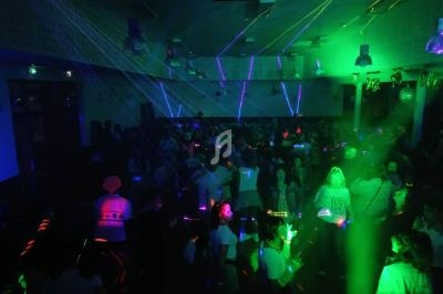 Des personnes dansent dans une salle sombre éclairée par des lumières laser vertes et violettes.