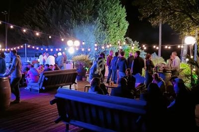 Groupe de personnes réunies en soirée en plein air, éclairées par des guirlandes lumineuses et des lampadaires.