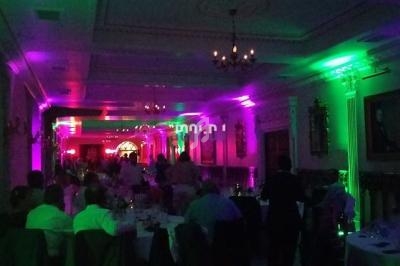 Salle de réception éclairée par des lumières colorées avec des invités assis à des tables.