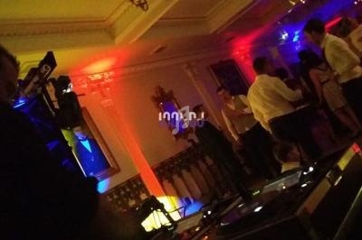 Personnes dansant dans une salle éclairée par des lumières colorées, avec un DJ et son équipement au premier plan.