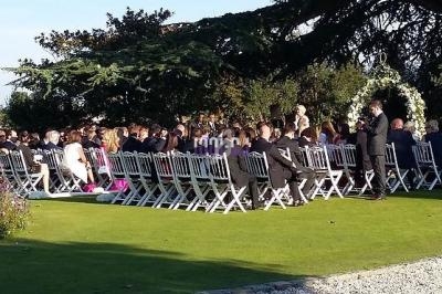 Cérémonie de mariage en plein air avec des invités assis sur des chaises blanches, entourés de verdure.