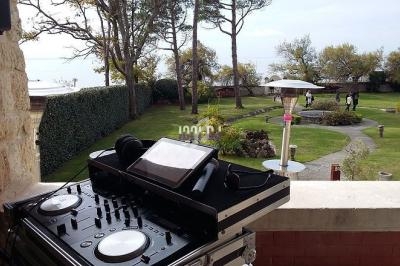 Table de mixage avec casque et tablette sur une terrasse surplombant un jardin avec arbres et sentiers.