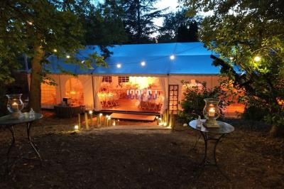 Tente éclairée en soirée dans un jardin, avec tables dressées à l'intérieur et guirlandes lumineuses suspendues.