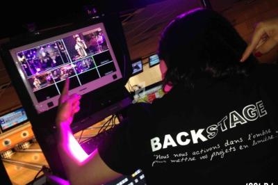 Une technicienne supervise des écrans de contrôle montrant des scènes de spectacle en coulisses.