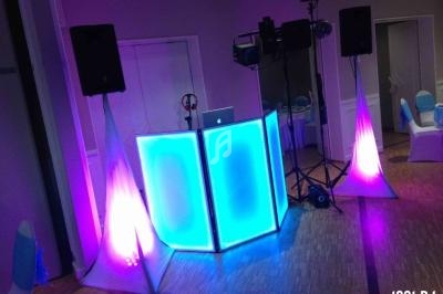 Poste de DJ avec une table lumineuse bleue, entourée de haut-parleurs et d'éclairages colorés dans une salle.