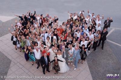 Un grand groupe de personnes rassemblées en extérieur, souriant et levant les bras, vu en plongée.