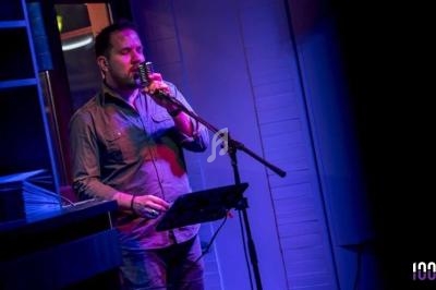 Homme chantant sur scène avec un micro, éclairé par des lumières colorées dans une ambiance sombre.