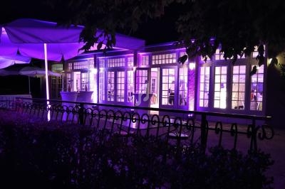 Façade d'un bâtiment éclairé par des lumières violettes, entouré de parasols et d'une clôture métallique, de nuit.