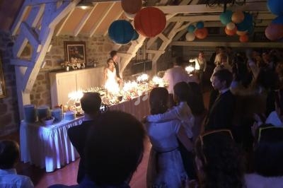 Un couple souffle des bougies sur un gâteau lors d'une fête dans une salle décorée de lanternes colorées.