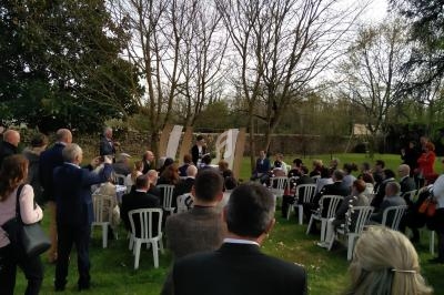 Cérémonie en plein air avec des invités assis sur des chaises blanches, entourés d'arbres et de verdure.